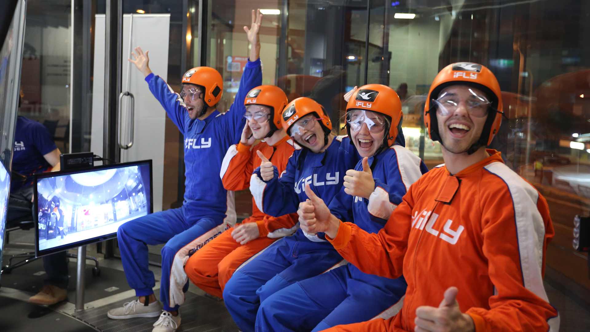 A group of adults wearing iFLY jumpsuits, cheering and excited to fly.